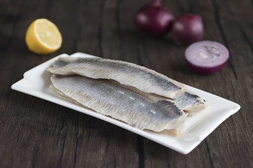 Herring fillets in a white plate on a dark wooden table.