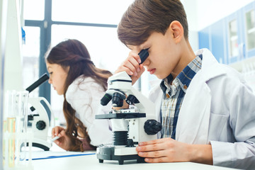 Little kids learning chemistry in school laboratory microscope project