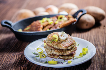 stacked fried potato cakes on white plate with sour cream, spring onion and chives