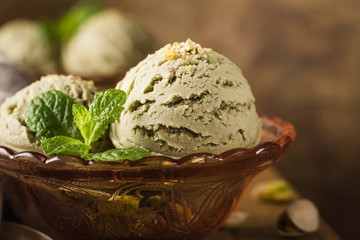 Pistachio ice cream scoops with grated pistachos in red glass bowl on old wooden table background. Homemade summer food concept with copy space.