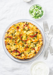 Potatoes and vegetables tortilla on a light background, top view. Potatoes, green beans, bell peppers, green peas, cheese, eggs casserole - a delicious breakfast or snack
