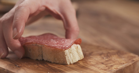 female hand make sandwich baguette slice with cream cheese and salami