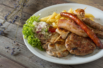 Balkan specialities - a plate of mixed meat including cevapi, pljeskavica, roasted pork neck and brisket.  on a wooden background. rustic food