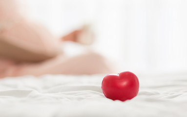 Red heart on the bed, Blurred background of pregnancy woman  in pink dress  in bedroom.