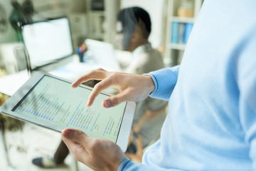 Close up of young web developer holding digital tablet with code lines in it while working on IT...