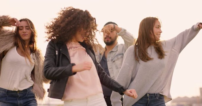 Medium shot of group of friends dancing together to music at sunset