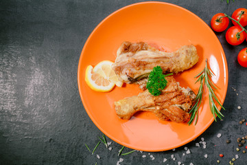 Grilled chicken legs with tomatoes and rosemary on a black plate on a stone,concrete  background