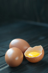 Eggs. Three fresh chicken eggs with one broken egg on dark rusti
