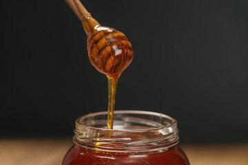 organic honey drips from wooden dipper in jar