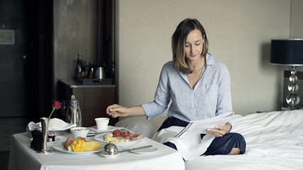 Young pretty businesswoman reading magazine and drinking tea during breakfast in hotel
- Powered by Adobe