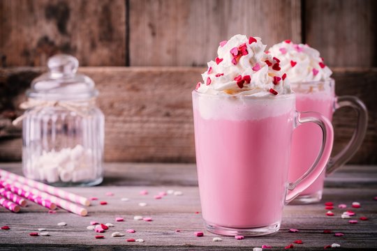 Pink hot milk with whipped cream and sugar hearts in a glass mug for Valentine Day