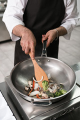 Chef showing off his professional skills. Cooking master at work in restaurant kitchen. Vegetables and meat mixing in the air technique