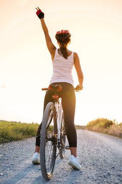 girl on a bicycle with a raised hand in the sunset