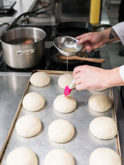 It is where a burger begins. A cook greasing hamburger rolls tops with egg before putting them in the oven and baking