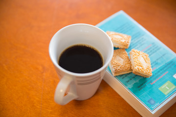 A cup of coffee with cookies and book on the table