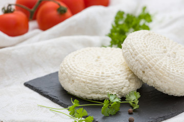 Closeup of round white homemade cheese - traditional milk creamy dairy product served with herbs and tomatoes on vintage black board. Rustic style.