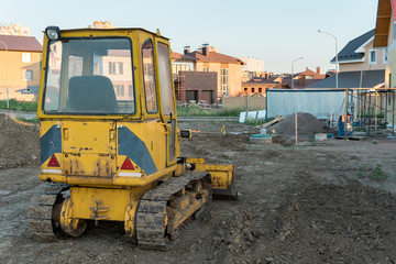 Fototapeta na wymiar Small yellow rear view bulldback view of small yellow bulldozer on the background of new private houses