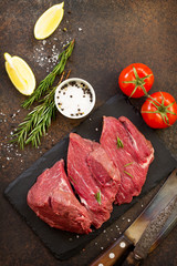Fresh meat. Raw steak beef on a slate cutting board, tomatoes, olive oil, spices and fresh rosemary on a stone table. Flat lay. Top view with copy space.