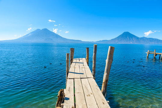Fototapeta Wooden pier at Lake Atitlan on the beach in Panajachel, Guatemala. With beautiful landscape scenery of volcanoes Toliman, Atitlan and San Pedro in the background. Volcano Highland in Central America.