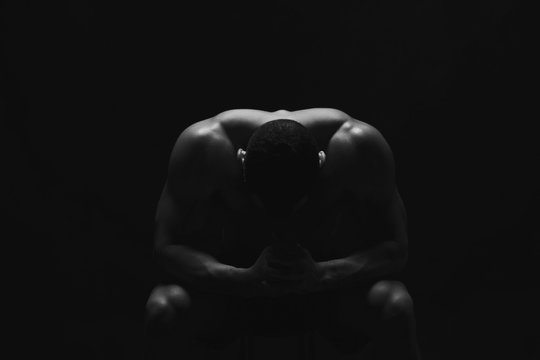 Male fitness model sitting at black studio background