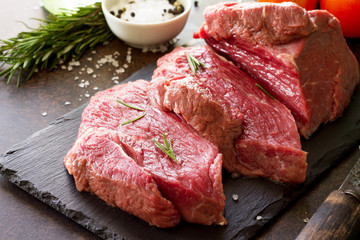 Fresh meat. Raw steak beef on a slate cutting board, tomatoes, olive oil, spices and fresh rosemary on a stone table.