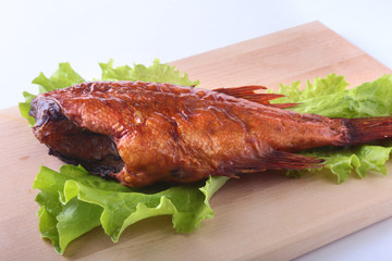 Smoked fish and lemon on green lettuce leaves on Wooden cutting board isolated on white background.