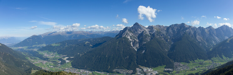 Panorama of a valley in Austria with a small town with green space all around. There are mountains as far as the eye can see.