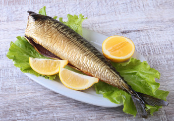 Smoked mackerele and lemon on green lettuce leaves on Wooden cutting board isolated on white background.