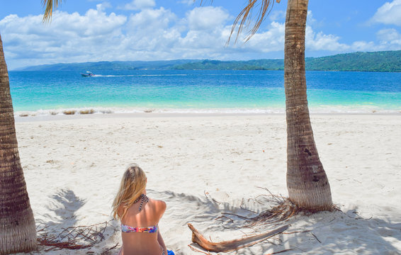 Frau sitzt im Bikini auf Handtuch mit dem R&uuml;cken zur Kamera am wei&szlig;en Sandstrand und schaut auf das Meer, Dominikanische Republik, Karibik, Samana