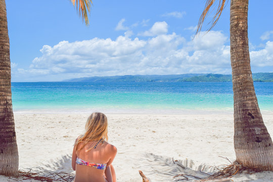 Frau von hinten sitzt am Strand im weißen Sand in der Karibik, Dominikanische Republik, und schaut auf  das türkis-farbene Meer