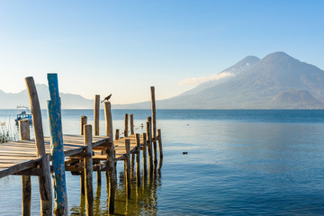 Fototapeta premium Wooden pier at Lake Atitlan on the beach in Panajachel, Guatemala. With beautiful landscape scenery of volcanoes Toliman, Atitlan and San Pedro in the background. Volcano Highland in Central America.