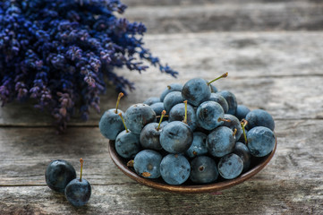 Autumn harvest blue sloe berries on a wooden table with a bouquet of lavender in the background. Copy space. Rustic style. - obrazy, fototapety, plakaty