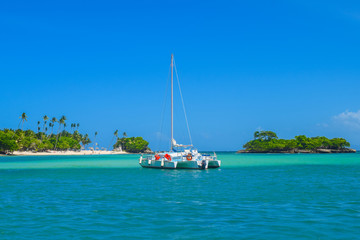 Katamaran in türkis-blauem Meerwasser, blauer Himmel, Insel mit weißem Sandstrand und Palmen im...