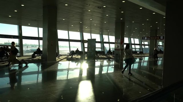 airport terminal interior, people travellers passengers silhouettes waiting in a lounge, hall view, beautiful background with sunshine, dolly shot from escalator