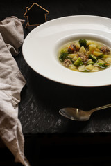 vegetable soup with meatballs and broccoli in a white plate