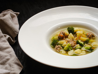 vegetable soup with meatballs and broccoli in a white plate