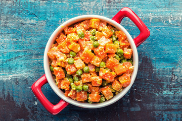 Carrot braised with fresh green peas in creamy milk sauce in stewpan, stewed vegetable saute, top view