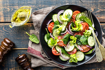 Healthy vegetable salad of fresh tomato, cucumber, spinach, onion and lettuce on plate. Diet menu. Top view.