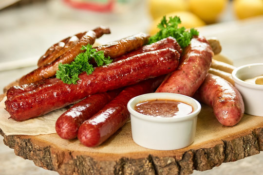 Served dish with assortment of sausages on wooden plate. Dish with assortment of grilled sausages, sauce and parsley on wooden plate.