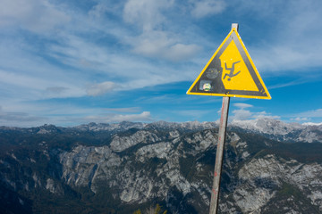 Warning sign for falling off a cliff or mountain. There are mountains in the background indicating the danger.