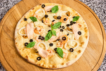 Pizza with seafood, olives and basil leaves. Round uncut pizza.