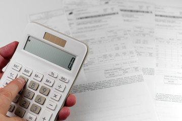 closeup on calculator in hand against bills in background