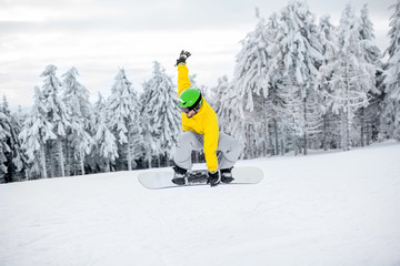 Man in colorful sports clothes riding the snowboard on the snowy mountains with beautiful trees on the background