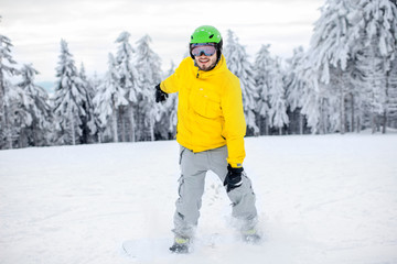Fototapeta na wymiar Man in colorful sports clothes riding the snowboard on the snowy mountains with beautiful trees on the background