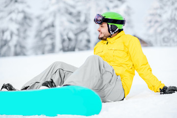 Fototapeta na wymiar Man sitting with snowboard resting after the riding outdoors at the snowy mountains