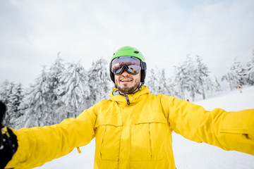 Fototapeta na wymiar Snowboarder in winter sports clothes making selfie photo outdoors at the snowy mountains