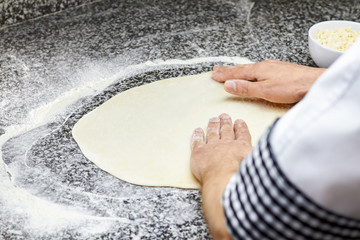 Kneading pizza dough. Pizza basis kneading. Hands preparing dough basis for pizza on the table.