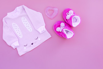 Cute pink baby clothes for girl. Shirt, booties, toy, bottle on pink background top view copy space