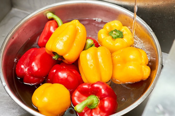 Red and yellow bell peppers in a basin of water, close up. Metal bowl with bell peppers.