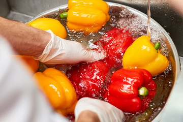 Close up chef hands washing papriks with water stream. Chef rinsing fresh vegetables under tap water.